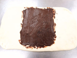 醇香巧克力吐司,拿出从冰箱冷冻好的面团，把巧克力酱均匀的涂抹在面团上，涂抹的长度大概是面团的1/2.放在面团的中央位置，涂抹均匀。