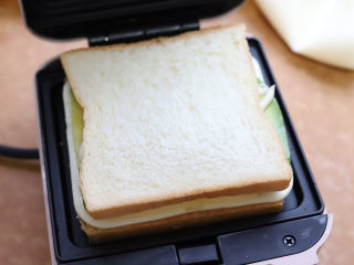 牛油果鸡蛋三明治,然后在表面再盖一层吐司面包。把面包和食材对整齐，用手顺带着扶一下吐司面包，把三明治机的盖子扣上，加热两三分钟就可以。