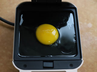 牛油果鸡蛋三明治,将三明治机预热，用耐高温的小刷子刷一层薄薄的油，磕入一个鸡蛋，扣上三明治机的盖子，加热两分钟。