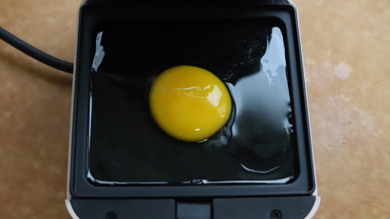 牛油果鸡蛋三明治,将三明治机预热，用耐高温的小刷子刷一层薄薄的油，磕入一个<a style='color:red;display:inline-block;' href='/shicai/ 9'>鸡蛋</a>，扣上三明治机的盖子，加热两分钟。