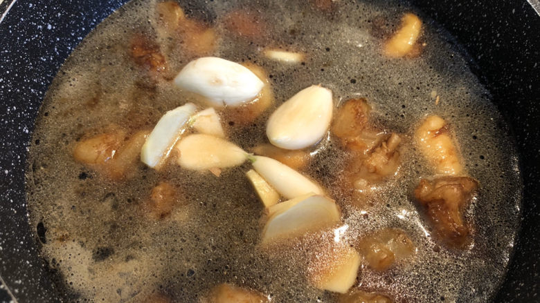 红烧牛蹄筋,翻炒均匀后，加入两大碗的水，要末过牛蹄筋，放入大蒜和姜片。大火煮开。