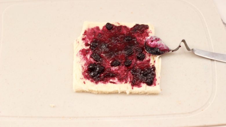 快手早餐-香蕉蓝莓吐司卷,在擀薄的吐司片上，均匀地抹上有颗粒的<a style='color:red;display:inline-block;' href='/shicai/ 2868'>蓝莓酱</a>。