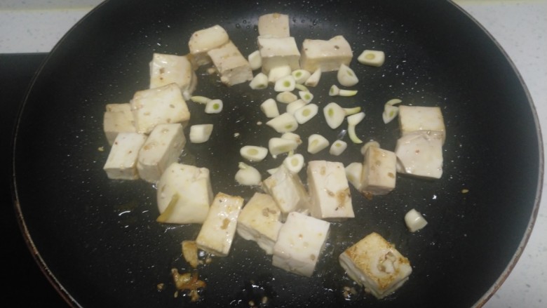 内酯豆腐炒平菇、鱼块,锅中放入适量油，放入豆腐煎至一面金黄，放入蒜瓣