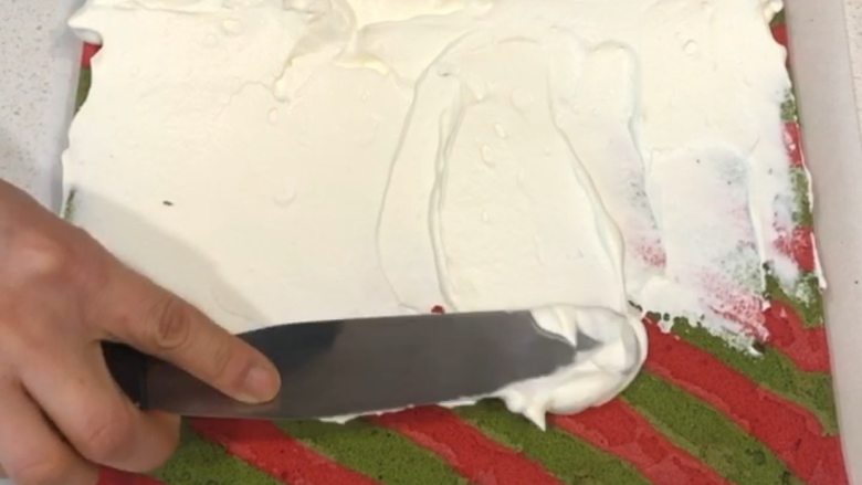 圣诞蛋糕卷,台面垫油纸，蛋糕卷正面朝上，将末端斜切一下，抹上打发好的蛋糕霜，