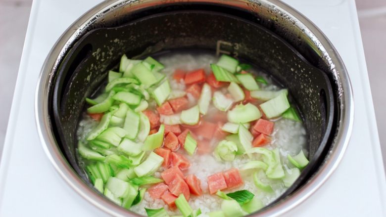 青口火腿青菜粥,烹饪至40分钟的时候，打开锅盖，锅中米粥已浓稠软烂了，这个时候先加入火腿丁和青菜的茎，盖上锅盖继续煮5分钟。