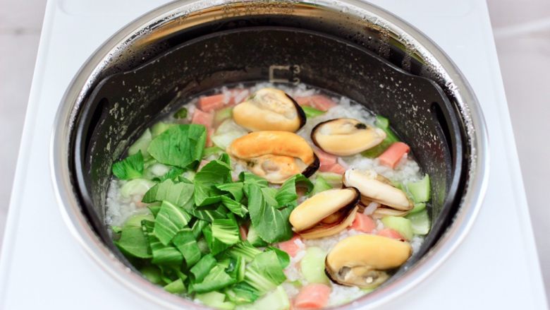 青口火腿青菜粥,再打开锅盖加入焯过水的青口和青菜叶。