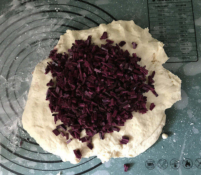 紫薯小馒头,案板上撒些干粉，拿出面团，按压排气后，把切好的紫薯丁放在上面
