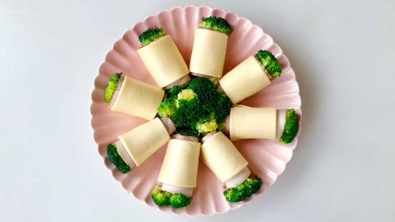 “花”开富贵——焗烤西兰花培根卷,将西兰花培根卷放入烤盘中，摆成花的造型;