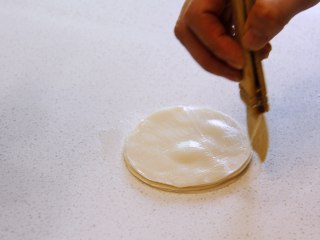 五彩福袋, 饺子皮表面刷油，然后层层叠起来，叠6-8层后用擀面杖向四周擀开成圆状，放入碟子中。