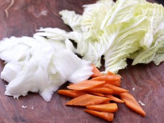 除夕必吃的炖菜，寓意年年有余,把大白菜叶和帮先分离，把帮斜切成薄片，叶切大片，胡萝卜切菱形片。
