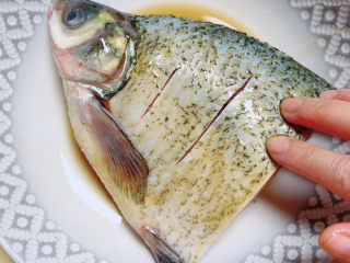 砂锅鱼头煲,先将半只鱼腌一下。放入盐、料酒、生抽。将调料在鱼表面和内部抹均匀。腌制10分钟。