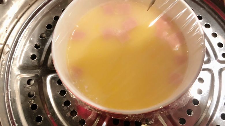 火腿蒸蛋,用保鲜膜封住蒸碗，用牙签在膜上戳细孔，轻轻戳，而后放入蒸锅中蒸熟