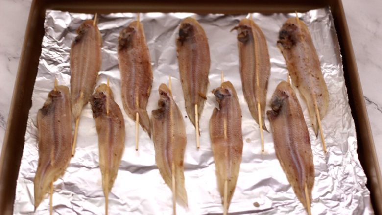 酱香辣烤舌头鱼,腌制好的鱼用竹签串起来，烤盘底下铺上锡纸，把串好的舌头鱼码放在烤盘里。
