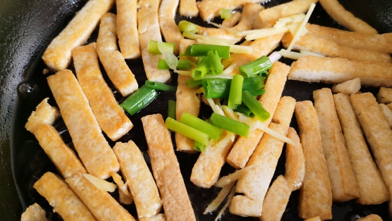 韭菜炒豆腐,豆腐煎好后放入葱姜，翻炒出香味。