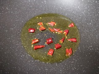 蒜苔炒牛肉卷,炒锅内倒适量的食用油烧热，将干红辣椒掰开下入爆香。