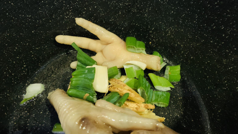 明虾鸡爪煲,锅里再加1勺油，鸡爪放入锅里，炒香，加蒜瓣大葱叶和姜片；