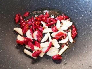 干煸芸豆,炒锅内留余油，下入蒜片、辣椒段和花椒。