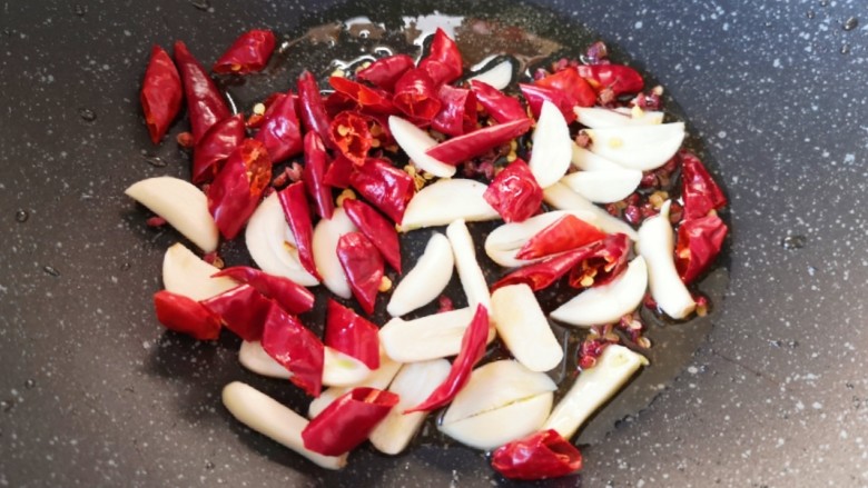 干煸芸豆,炒锅内留余油，下入蒜片、辣椒段和花椒。