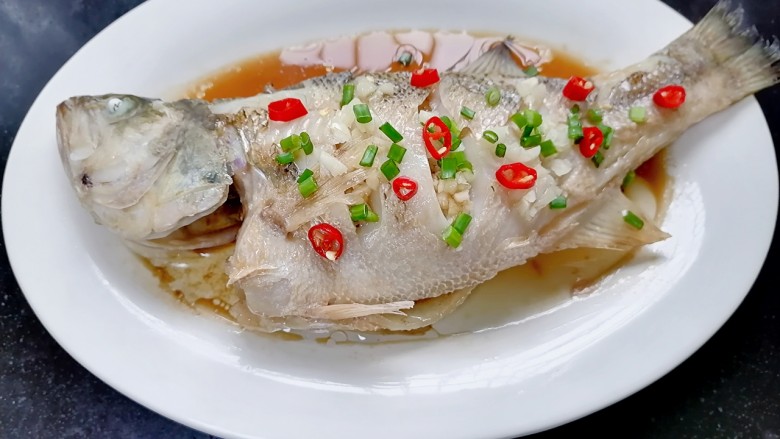 葱油鲈鱼,将热的葱油浇在鱼上然后撒上葱花和小米辣
