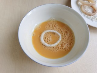 黄金鱿鱼圈,将沾好淀粉的鱿鱼圈放入蛋液中，沾上一层蛋液。