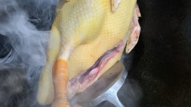 白切鸭,一手拿鸭爪一手用铲子把鸭子大腿部分来回摩擦锅面，让表面出油而焦黄。