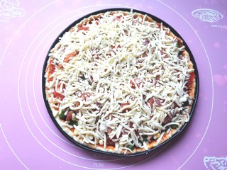 培根披萨,接着均匀的放上洋葱，青红椒丝，培根腊肠，上面再铺上一层厚厚的芝士，这样会更拉丝