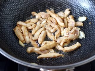 芦笋炒鸡肉条,锅烧热后，倒入花生油，油热后先爆香大蒜片，再放入切条的鸡肉。大火快速翻炒。