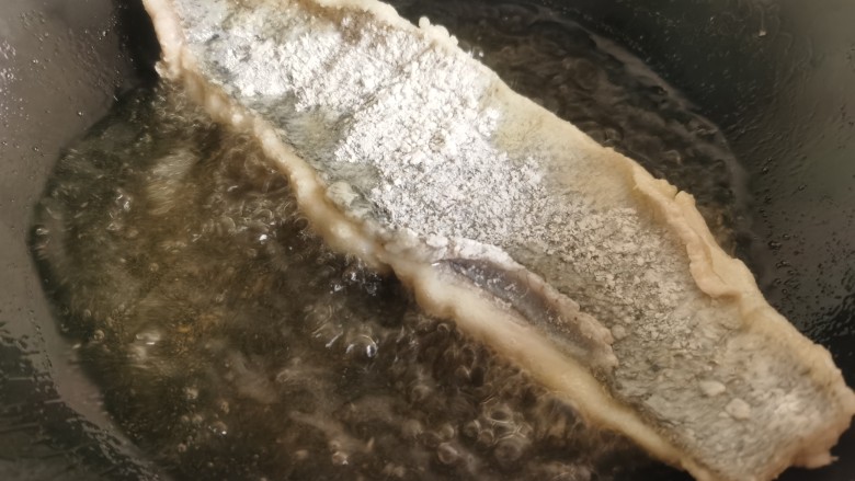 糖醋鲈鱼,锅里放油烧热，将鱼肉朝下放入油锅里炸制。