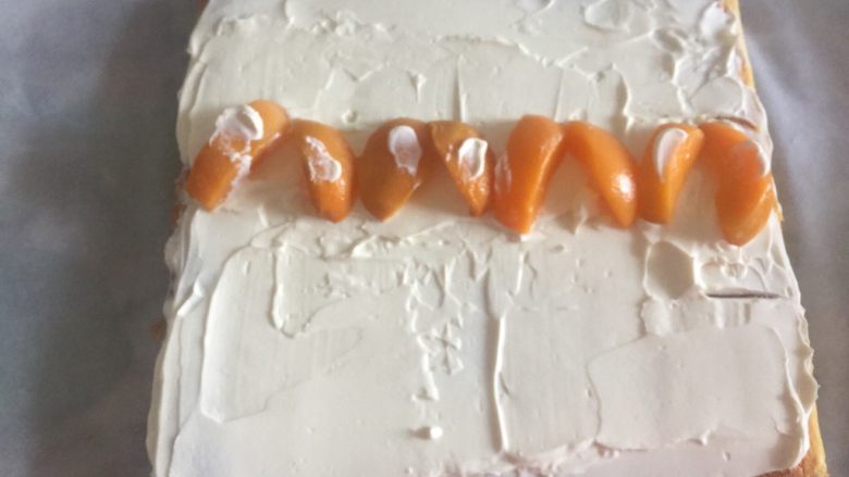 黄桃奶油蛋糕卷,制作的是反卷O形卷，焦色那面朝上，淡奶油抹匀，中间抹成小山丘，摆放大颗粒水果果肉。