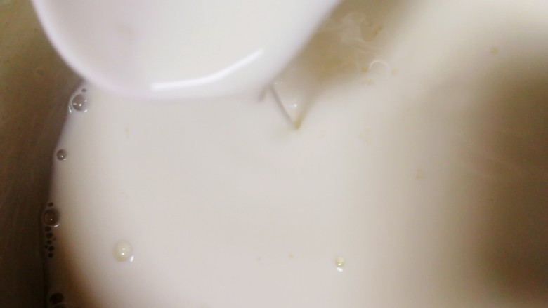 椰奶小方【零失败】,把牛奶玉米淀粉液一点一点加入热奶锅里，不断搅拌推动奶锅底部。