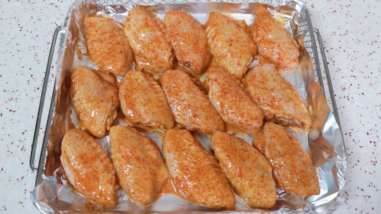 蒜香炸鸡翅,炸篮里铺上锡纸，刷上一层食用油，将腌制好的鸡翅摆在上面。