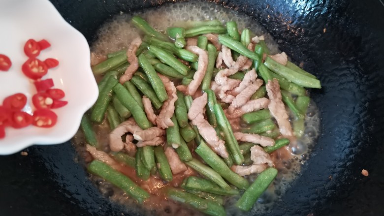 四季豆炒肉,倒入小米辣大火烧1分钟，烧至汤汁粘稠，加入少许鸡精提鲜
