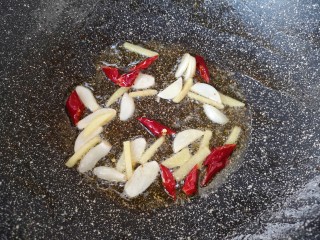 四季豆炒肉,锅里倒入适量食用油烧热，下入大蒜、生姜和干红辣椒炒香。