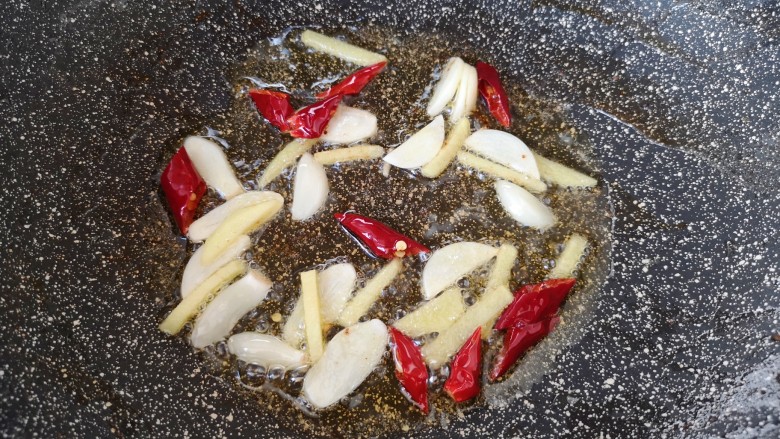 四季豆炒肉,锅里倒入适量食用油烧热，下入大蒜、生姜和干红辣椒炒香。