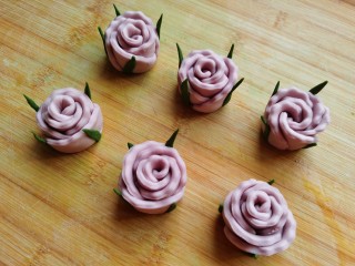 紫薯玫瑰花馒头,绿色面团搓成细条，稍微压扁，抹上少许水，如上图一样十字摆放，把玫瑰花放在上面，粘在花朵四周即可。