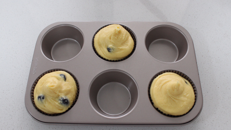 蓝莓玛芬蛋糕,均匀挤满玛芬模具，（放一个纸托，再把纸托放入模具），一定要挤满，并且还要高于模具。因为烤的过程中会变大，所以要交错来放，以上配料是三个的量。