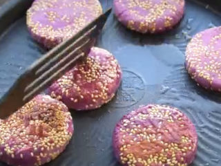 紫薯芝麻饼,煎得一面泛黄了，翻面继续煎，全程多翻几次，也可以盖上盖子小焖一会，这样熟得快