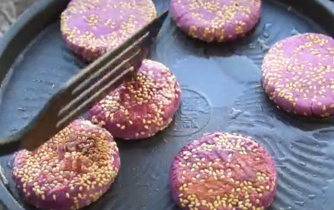 紫薯芝麻饼,煎得一面泛黄了，翻面继续煎，全程多翻几次，也可以盖上盖子小焖一会，这样熟得快