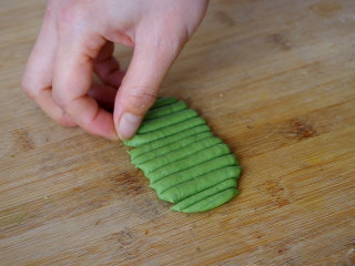 胡萝卜馒头,用擀面杖把绿色面团擀成薄片，厚度约0.4CM左右，用刮板切成竖条。