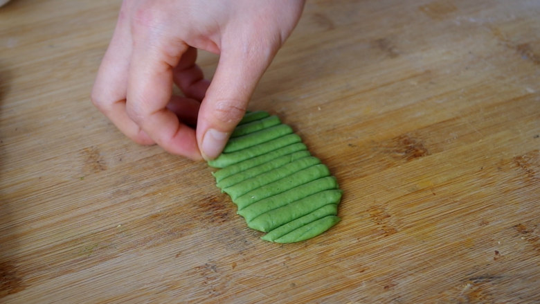 胡萝卜馒头,用擀面杖把绿色面团擀成薄片，厚度约0.4CM左右，用刮板切成竖条。