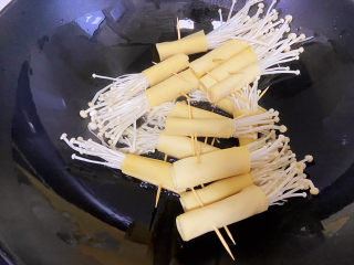 豆皮金针菇卷,锅中倒适量的油，油热改中小火，将金针菇放入锅中，两面都煎一下。
