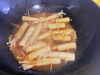 豆皮金针菇卷,大火煮开后改小火，直到汤汁浓稠以后，就可以关火了，这是个准备好盘子，用筷子把豆皮卷夹到盘中摆盘，并将牙签取下来。