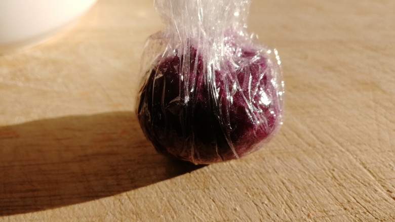 紫薯芝麻饼,挖一汤匙紫薯，放在保鲜膜上，包紧成球。