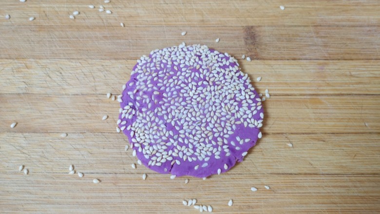 紫薯芝麻饼,放在案板上用擀面杖轻轻擀一下，让芝麻牢牢的粘在紫薯饼上，不易脱落。