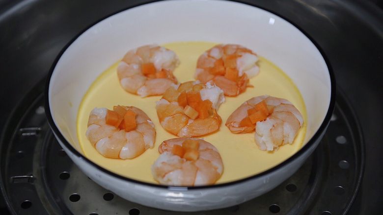 虾仁蒸蛋羹,十分钟后将虾摆入蛋羹碗中，中间摆上胡萝卜粒，继续蒸5分钟