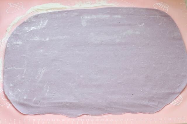 紫薯小馒头,操作台撒干面粉防粘，取出面团揉匀擀成长方形的面片，下面边缘处擀薄。