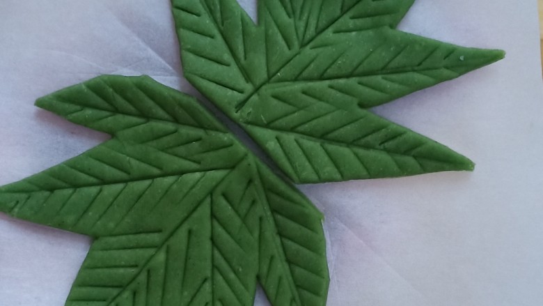 紫薯小馒头（葡萄馒头）,取绿色面团，擀成薄片，用刀切出叶子的轮廓，再把叶片的纹路压出来。做4片，流出一丢丢的绿色面团搓成1毫米粗的细条作为藤