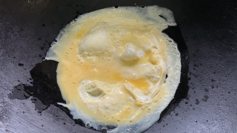 酸豆角炒鸡蛋,旋转油锅，让蛋液顺着边沿延展来了。两边煎熟后出锅。