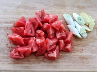 红烧牛腩,西红柿去蒂后在顶部划十字刀，然后放入开水中烫约二十秒，捞出撕掉外皮切滚刀块。大葱切段，姜切小片。