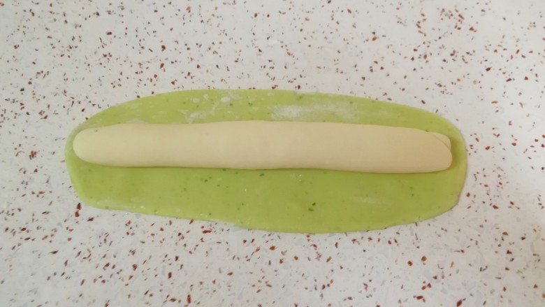 猪肉白菜水饺,白色的长条状面团放在绿色的长方形面团上，卷起来。 